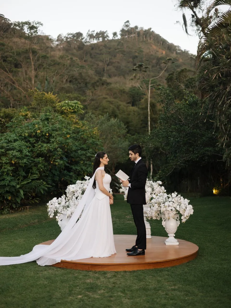 Noivos trocando votos ao ar livre sobre palco circular de madeira